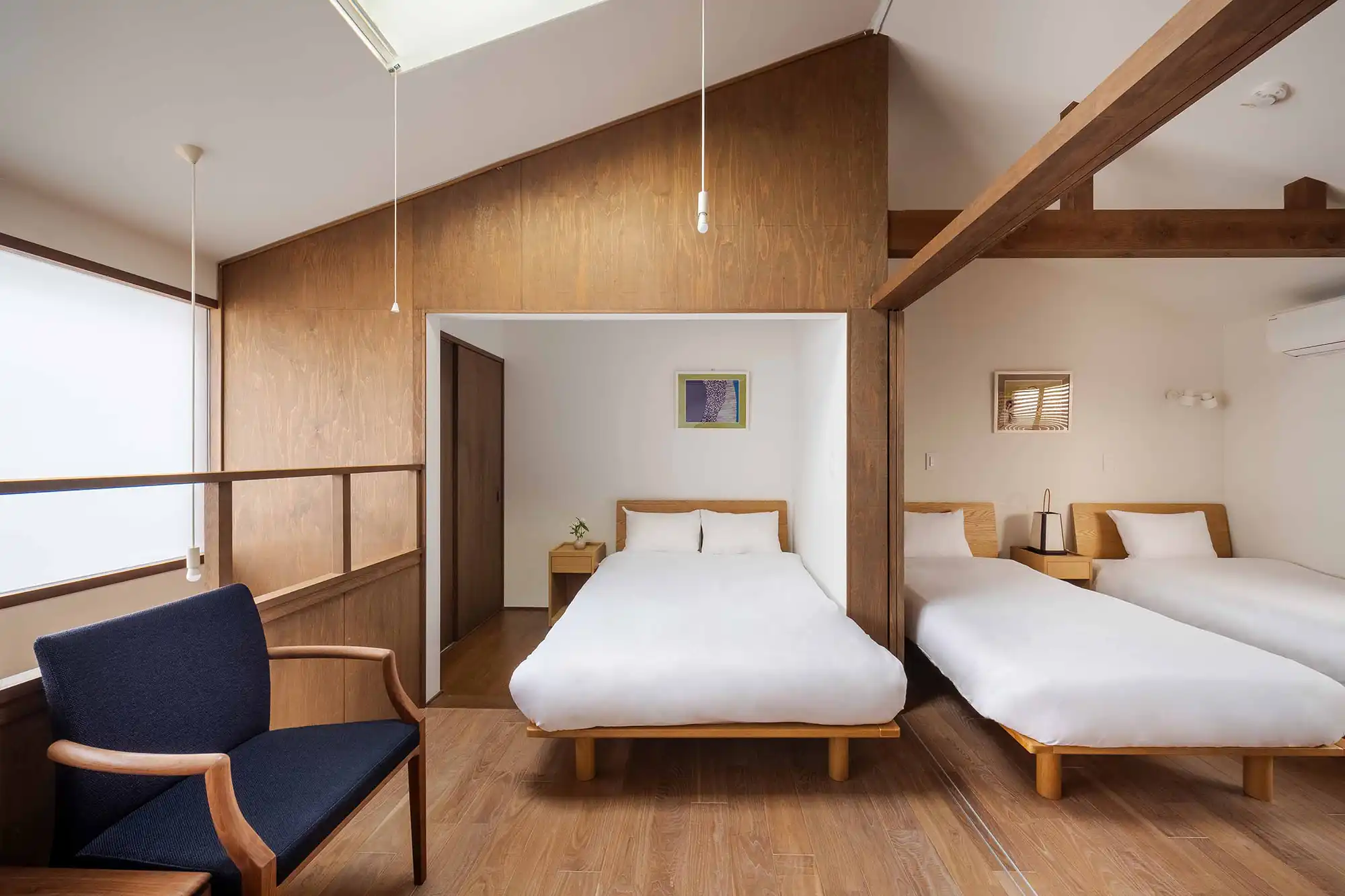 Three Western-style beds in a traditional Japanese house, featuring a skylight, exposed wooden beams, natural wood accents, and large windows that fill the space with natural light.